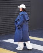 بارونی زنانه بلند دمسه دوزی سرمه ای آستر دار با کمربند و فلاپ پشت نمای نیم رخ در فضای شهری