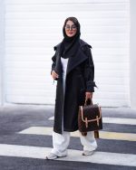 بارونی زنانه بلند مشکی دمسه دوزی کمربنددار یقه برگردان نمای تمام قد استایل شهری روی ست روشن