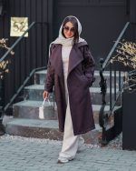 بارونی زنانه بلند دمسه دوزی رنگ شکلاتی کمربنددار یقه برگردان نمای تمام قد در فضای شهری