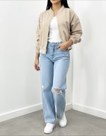 بامبر زنانه کرم روشن فیت آزاد یقه کشی روی تاپ سفید با شلوار جین راسته زانو زاپ دار و کتانی سفید نمای تمام قد